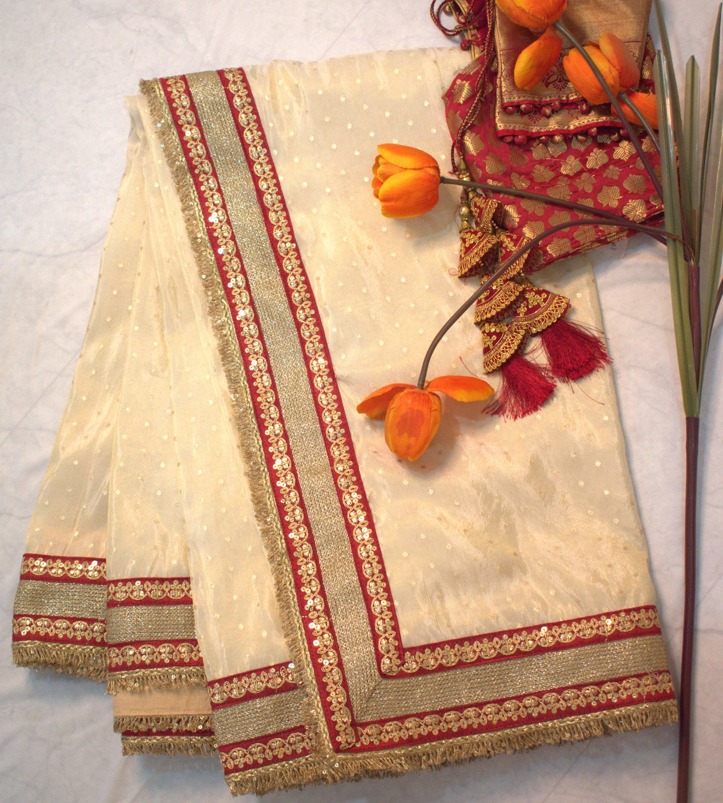 IVORY TISSUE SAREE WITH HEAVY MAROON ZARI BORDER AND FRINGE DETAILING.